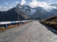 a cobbled road runs along a narrow side of a mountain range with mountains in the background