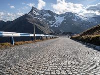 a cobbled road runs along a narrow side of a mountain range with mountains in the background