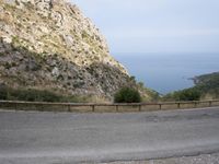 a winding road is shown on a mountain side near the ocean, and a hill with mountains and sea beyond