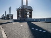 two people walking along a road near large power plants, with water visible from them