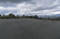this is a parking lot with trees and mountains in the background behind it with a car driving along the road and a cloudy sky