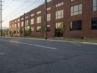 an empty street in front of a large red brick building on the other side of the road is a street light that has a line for motorists