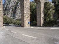 a road in front of a bridge that goes to the mountains with a blue sign on it