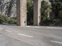 a road in front of a bridge that goes to the mountains with a blue sign on it