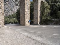 a road in front of a bridge that goes to the mountains with a blue sign on it