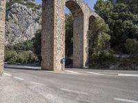 a road in front of a bridge that goes to the mountains with a blue sign on it