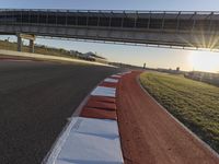 a road and a bridge over a hill on a clear day at sunrise with light reflected on the pavement