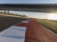 a road and a bridge over a hill on a clear day at sunrise with light reflected on the pavement