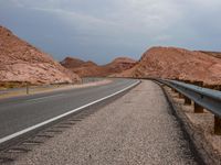 an empty road in the desert with a few mountains in the background and a sky overhead