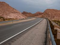 an empty road in the desert with a few mountains in the background and a sky overhead