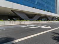 an office building with a large sidewalk and some white arrow signs on the asphalt of the road