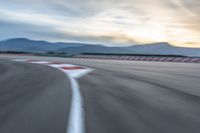 a photo of a dirt race track with sun setting in the distance of the track