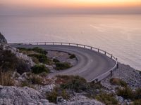 the road curves into the water while it stretches into the distance from a cliff on the island of capo de mielo in portugal