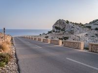 a winding road near the ocean at dusk with rocks on each side of the road