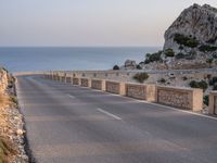 a winding road near the ocean at dusk with rocks on each side of the road