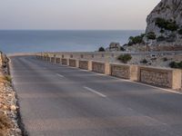 a winding road near the ocean at dusk with rocks on each side of the road