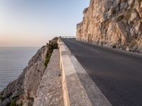 a road leading into a cliff with the ocean in the back ground and a building in the corner