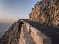 a road leading into a cliff with the ocean in the back ground and a building in the corner