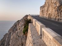 a road leading into a cliff with the ocean in the back ground and a building in the corner