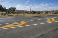 a street is seen with a yellow arrow painted on the side of it, and telephone poles in the distance