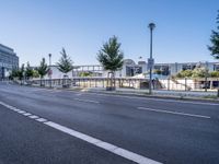 the empty road stretches across to a city street with buildings in the background and fenced off