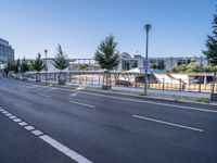 the empty road stretches across to a city street with buildings in the background and fenced off