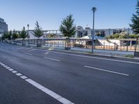 the empty road stretches across to a city street with buildings in the background and fenced off