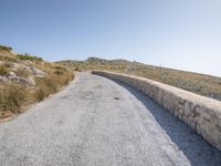 a road with grass next to a hill on a sunny day in the sunshine on top of the mountain