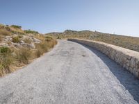 a road with grass next to a hill on a sunny day in the sunshine on top of the mountain