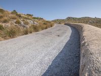 a road with grass next to a hill on a sunny day in the sunshine on top of the mountain