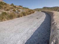 a road with grass next to a hill on a sunny day in the sunshine on top of the mountain