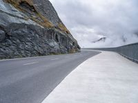 a lone motor cycle on the road near mountains with fog in the air with low clouds