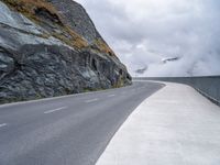 a lone motor cycle on the road near mountains with fog in the air with low clouds