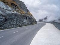 a lone motor cycle on the road near mountains with fog in the air with low clouds