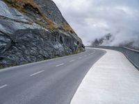 a lone motor cycle on the road near mountains with fog in the air with low clouds