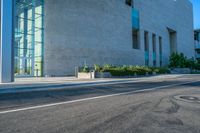 the side of an empty city street next to a building with a large glass wall