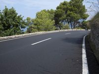 a black asphalt road with white markings and some trees on either side of it and a blue sky