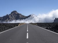 a highway that has some mountains in the background, and mist rising behind it and blue skies