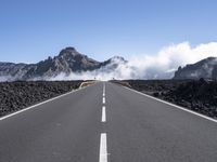 a highway that has some mountains in the background, and mist rising behind it and blue skies