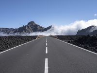 a highway that has some mountains in the background, and mist rising behind it and blue skies