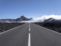 a highway that has some mountains in the background, and mist rising behind it and blue skies