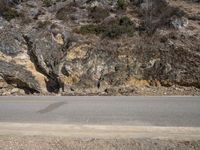 the sidewalk and road near the rocky mountain side with a motorcycle parked on it in front of it