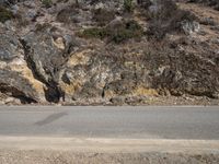 the sidewalk and road near the rocky mountain side with a motorcycle parked on it in front of it