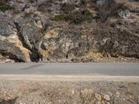 the sidewalk and road near the rocky mountain side with a motorcycle parked on it in front of it