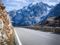 a view of a mountain road going down to a mountain peak with snow capped peaks in the background