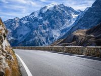 a view of a mountain road going down to a mountain peak with snow capped peaks in the background