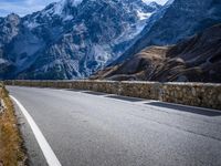 a view of a mountain road going down to a mountain peak with snow capped peaks in the background