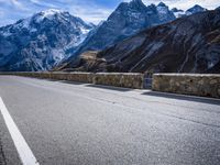 a view of a mountain road going down to a mountain peak with snow capped peaks in the background