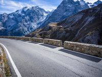 a view of a mountain road going down to a mountain peak with snow capped peaks in the background