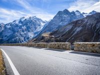 a view of a mountain road going down to a mountain peak with snow capped peaks in the background